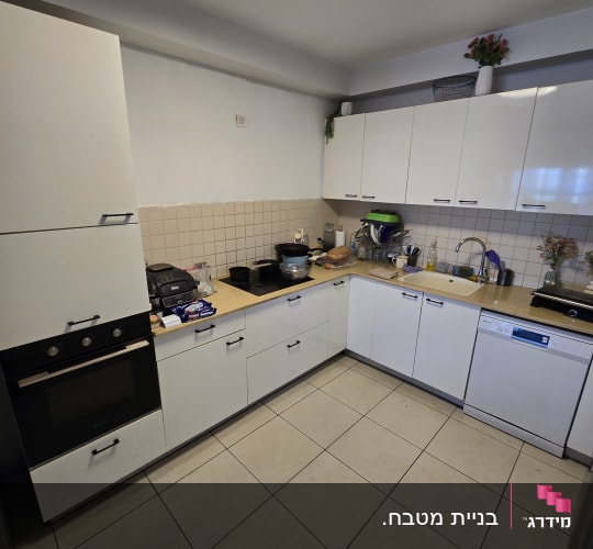 מטבח עם ארונות לבנים וכלי מטבח על השיש